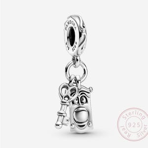 May include: A silver charm with a key and a door design, suspended from a Pandora branded bail. The charm has intricate detailing and a shiny finish. The charm is a piece of jewellery.