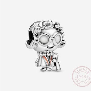 Può includere: Un charm in argento sterling raffigurante un personaggio dei cartoni animati con capelli ricci, occhiali rotondi e un vestito. Il charm ha una piccola borsa e un accento rosso-arancio sull'abito. È timbrato con "Sterling 925 Silver".