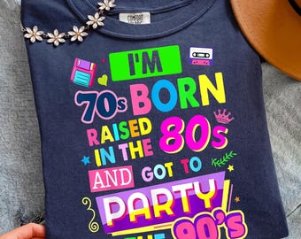 May include: Navy blue t-shirt with the text "I'm 70s Born, Raised in the 80s, and Got to Party in the 90s" in colorful retro fonts. The shirt features graphics of a floppy disk, cassette tape, and a crown.
