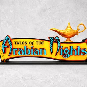 Könnte beinhalten: Dekoratives Schild mit dem Text "Tales of the Arabian Nights". Das Schild hat ein gelbes Banner mit roten und schwarzen Verzierungen und eine goldfarbene Wunderlampe. Der Sockel ist schwarz.