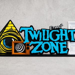 Könnte beinhalten: Eine dekorative Skulptur mit Elementen aus der Twilight Zone. Sie enthält eine gelbe Pyramide mit einem Auge, einen Retro-Fernseher mit einer Spirale, das Logo der Show und eine weiße Tür. Der Text "E=mc²" ist ebenfalls vorhanden.