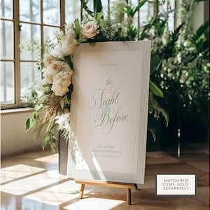 Puede incluir: Un letrero de bienvenida para una boda, con el texto "Welcome to the Night Before" en una elegante escritura. El letrero est&aacute; sobre un caballete de madera, rodeado de flores blancas y vegetaci&oacute;n. Tambi&eacute;n incluye los nombres de la pareja y el lugar.