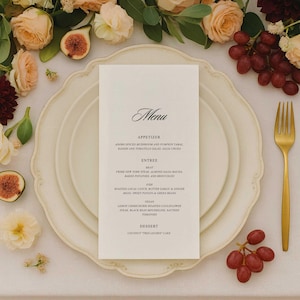 Może przedstawiać: Formalne nakrycie stołu z białą kartą menu, złotym widelcem i dekoracyjną kompozycją kwiatową. Menu zawiera opcje przystawek, dań głównych i deserów. Obecne są również figi i winogrona.