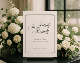 Puede incluir: Un letrero conmemorativo con el texto "In Loving Memory" en escritura elegante, enmarcado con un borde gris. El letrero se muestra sobre un soporte negro, rodeado de rosas blancas y vegetación. El texto incluye nombres.