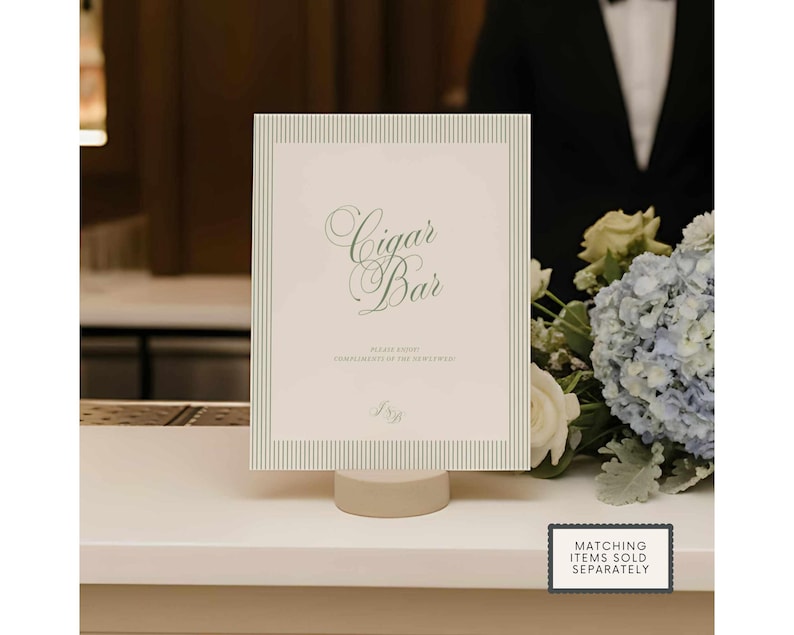 Puede incluir: Un letrero rectangular con las palabras "Cigar Bar" en escritura elegante, enmarcado por un borde a rayas. El letrero est&aacute; apoyado en un peque&ntilde;o soporte redondo beige. Un ramo de flores est&aacute; en el fondo.