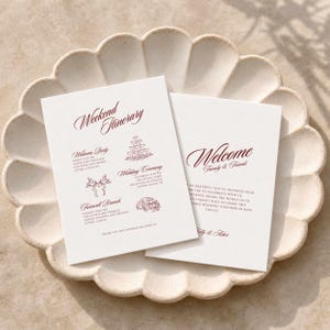 Könnte beinhalten: Zwei weiße, rechteckige Hochzeitskarten mit dunkelrotem Text und Strichzeichnungen. Eine Karte trägt den Titel Weekend Itinerary und beschreibt eine Welcome Party, Wedding Ceremony und Farewell Brunch. Die zweite Karte ist mit Welcome Family & Friends betitelt.
