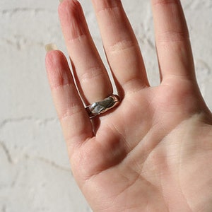 K&ouml;nnte beinhalten: Ein silberner Ring mit einer strukturierten, geh&auml;mmerten Oberfl&auml;che. Der Ring wird am Ringfinger einer Hand getragen.