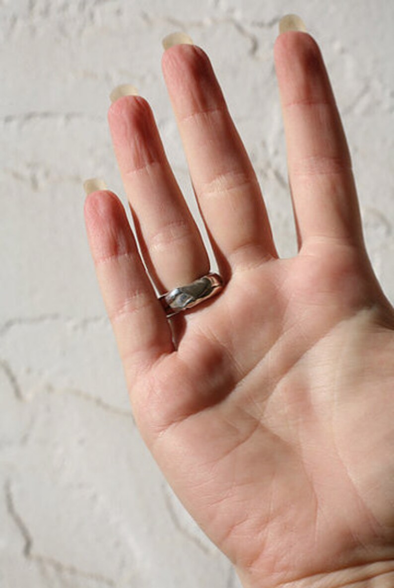 K&ouml;nnte beinhalten: Ein silberner Ring mit einer strukturierten, geh&auml;mmerten Oberfl&auml;che. Der Ring wird am Ringfinger einer Hand getragen.