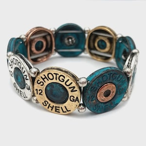 Könnte beinhalten: Ein Armband aus recycelten Schrotpatronen. Das Armband zeigt eine Mischung aus silbernen, kupferfarbenen und goldfarbenen Metallhülsen mit türkisfarbenen Akzenten. Jede Hülse ist mit "SHOTGUN 12 SHELL" beschriftet.