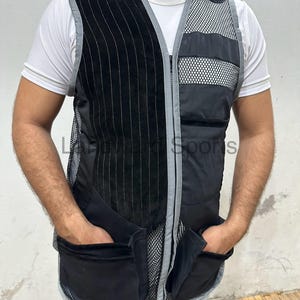 Puede incluir: Un chaleco de tiro negro y gris con un panel de malla y múltiples bolsillos. El chaleco tiene una cremallera y un ribete blanco.