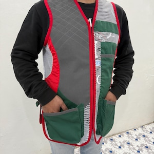 May include: A red, gray, and green hunting vest with a mesh front and multiple pockets. The vest has a zipper closure and a red trim.