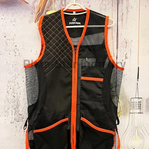 Könnte beinhalten: Eine schwarze Weste mit leuchtend orangefarbenen Kanten, einem gesteppten Muster auf der rechten Brust, Netzeinsätzen an den Seiten und oben links sowie zwei großen Vordertaschen. Das Innenetikett zeigt den Text "PLATA-STAR" mit einem Sternsymbol.
