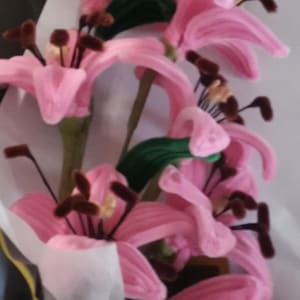 May include: A bouquet of pink felt lilies with brown felt stamens. The lilies are arranged in a white paper wrapper.