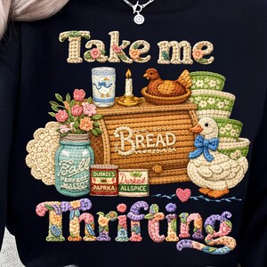 Pu&ograve; includere: Felpa nera con un design ricamato colorato. Il design include il testo "Take me Thrifting" con immagini di una cassetta del pane, un'anatra, fiori e barattoli. La felpa ha un girocollo.