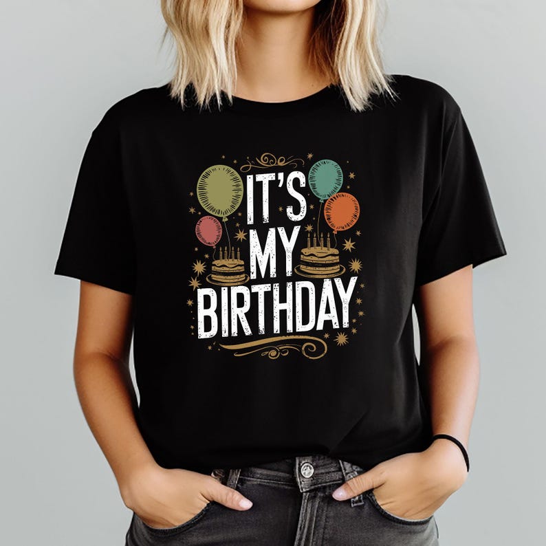 May include: Black t-shirt featuring the text "IT'S MY BIRTHDAY" in white, accompanied by colourful balloon and cake graphics. The design includes a gold decorative flourish. A fun tee for birthday celebrations.