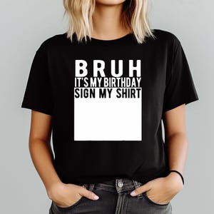 May include: Black t-shirt with the white text "BRUH IT'S MY BIRTHDAY SIGN MY SHIRT". A large white rectangle is below the text, for signatures. The t-shirt is short-sleeved and a casual style.