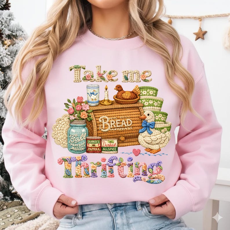 Pu&ograve; includere: Felpa rosa chiaro con la scritta "Take me Thrifting" in un carattere ricamato colorato. La grafica include una cassetta del pane, un'anatra, fiori e barattoli. Il design ha un'estetica vintage e fatta in casa.