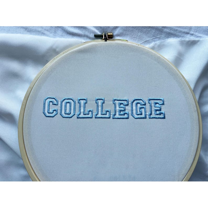 K&ouml;nnte beinhalten: Ein wei&szlig;er Stickrahmen mit dem Wort "COLLEGE" in blauer Stickgarn gestickt.