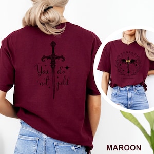 May include: Maroon t-shirt with a black sword graphic and the text "You do not yield." A smaller image shows a similar shirt with a circular design and the text "Basgiath War College."