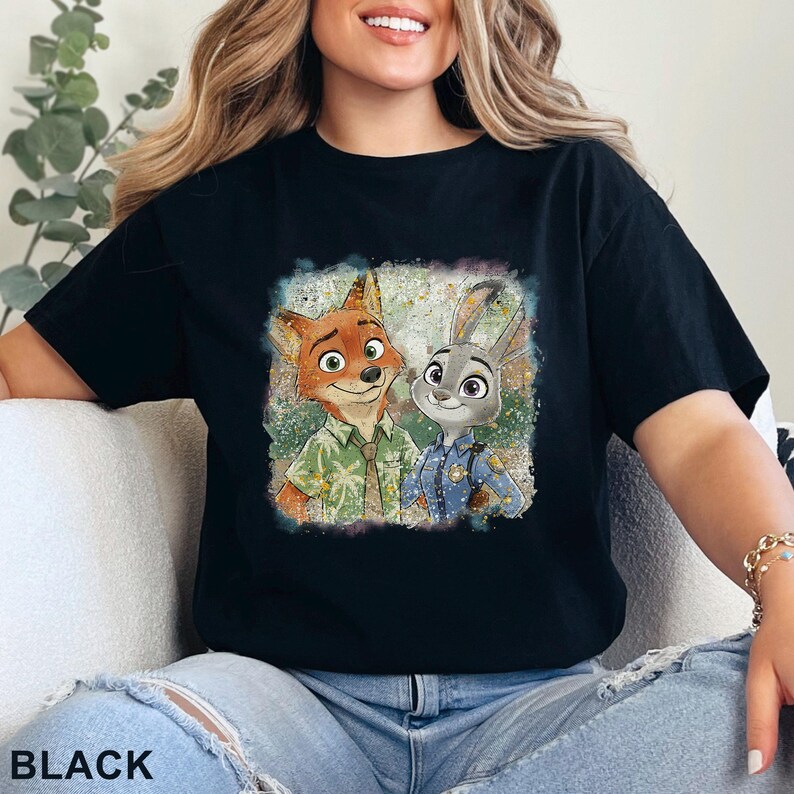 K&ouml;nnte beinhalten: Schwarzes T-Shirt mit einer farbenfrohen Grafik von Nick Wilde und Judy Hopps aus Zootopia. Die Charaktere sind in einem quadratischen Design dargestellt. Das Wort "BLACK" ist unten auf dem Shirt aufgedruckt.