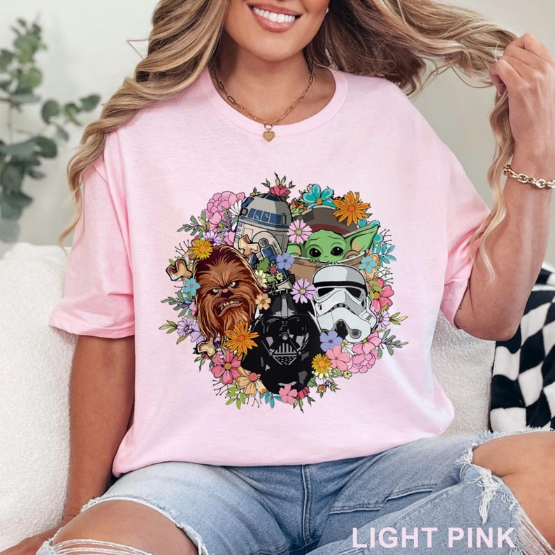 Puede incluir: Camiseta rosa claro con un dise&ntilde;o floral con personajes de Star Wars, incluyendo Darth Vader, un Stormtrooper, Chewbacca, R2-D2 y Grogu. El texto "LIGHT PINK" est&aacute; en la parte inferior de la camiseta.