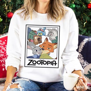 Peut inclure: Sweat-shirt blanc avec un motif rectangulaire repr&eacute;sentant des personnages du film d'animation "Zootopia". Le motif comprend Judy Hopps, Nick Wilde et d'autres personnages. Le mot "Zootopia" est imprim&eacute; en noir.