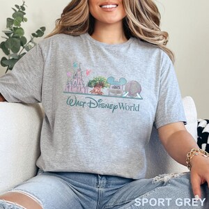 May include: Sport grey t-shirt featuring a colorful graphic of Walt Disney World landmarks, including a castle, tree, and Spaceship Earth. The text "Walt Disney World" is printed below the graphic in a script font.
