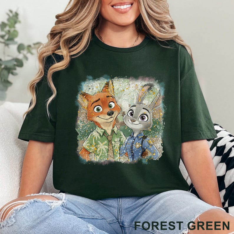 K&ouml;nnte beinhalten: Forstgr&uuml;nes T-Shirt mit einer farbenfrohen Grafik von Nick Wilde und Judy Hopps aus Zootopia. Das Bild zeigt die l&auml;chelnden Fuchs- und Hasenfiguren. Der Text "FOREST GREEN" ist am unteren Rand des T-Shirts aufgedruckt.