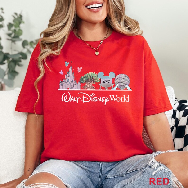 May include: Red t-shirt featuring a graphic of the Walt Disney World logo with iconic park imagery. The design includes Cinderella's castle, the Tree of Life, Mickey Mouse ears, and Spaceship Earth. The word "Studios" is also visible.