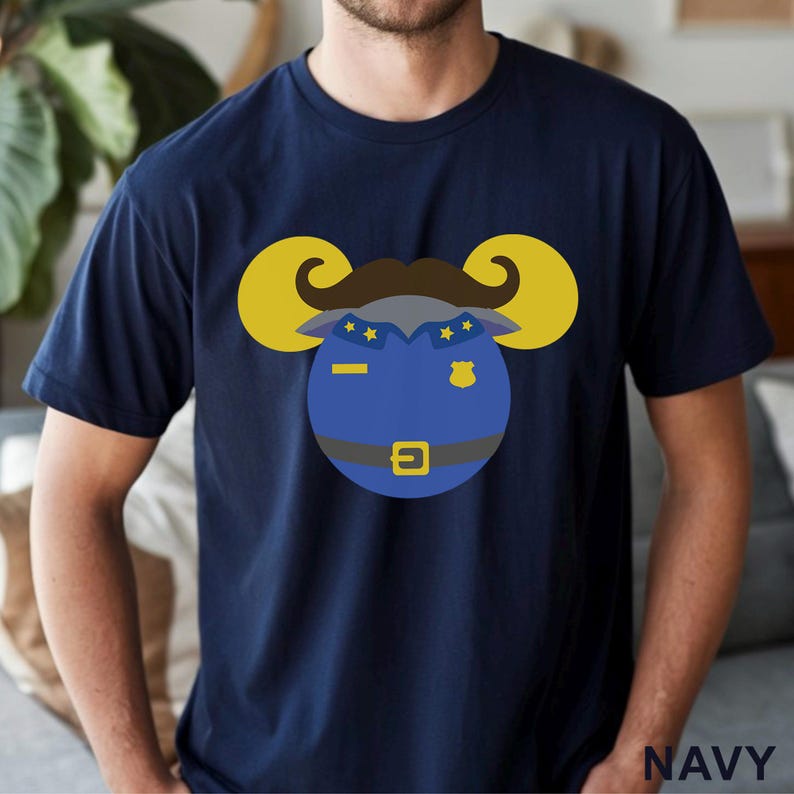 Puede incluir: Camiseta azul marino con un dise&ntilde;o de carnero de dibujos animados con uniforme de polic&iacute;a. El carnero tiene cuernos amarillos, bigote marr&oacute;n y uniforme azul. La palabra "NAVY" est&aacute; impresa en blanco en la esquina inferior derecha.