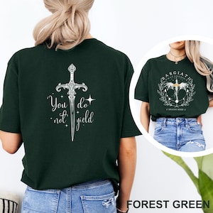 May include: Forest green t-shirt with a white sword graphic and the text "You do not yield" on the back. Another shirt in the image has a circular design with text. The shirt is a casual wear item.