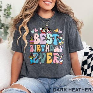 May include: Dark heather gray t-shirt with the words "BEST BIRTHDAY EVER" in colorful bubble letters. The design includes cartoon characters and birthday-themed graphics. The shirt is a casual style.