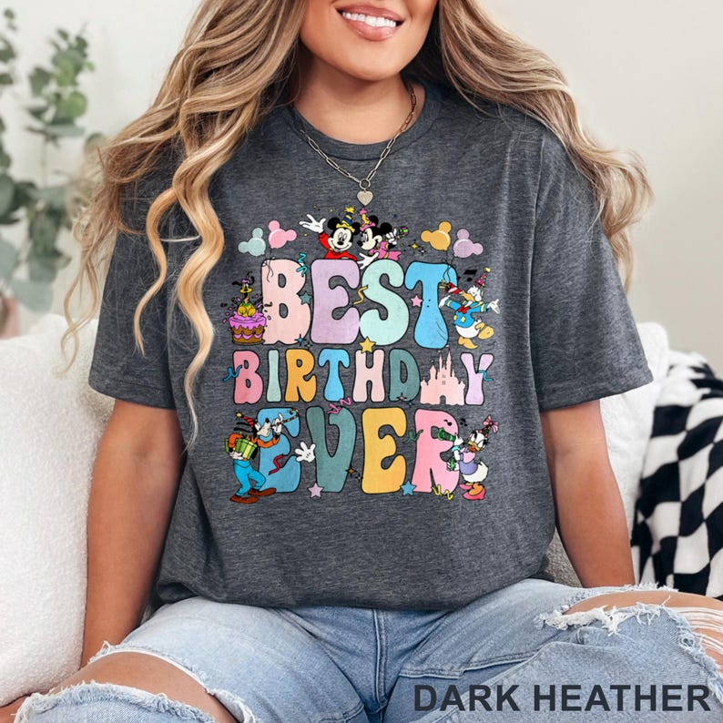 May include: Dark heather gray t-shirt with the words "BEST BIRTHDAY EVER" in colorful bubble letters. The design includes cartoon characters and birthday-themed graphics. The shirt is a casual style.