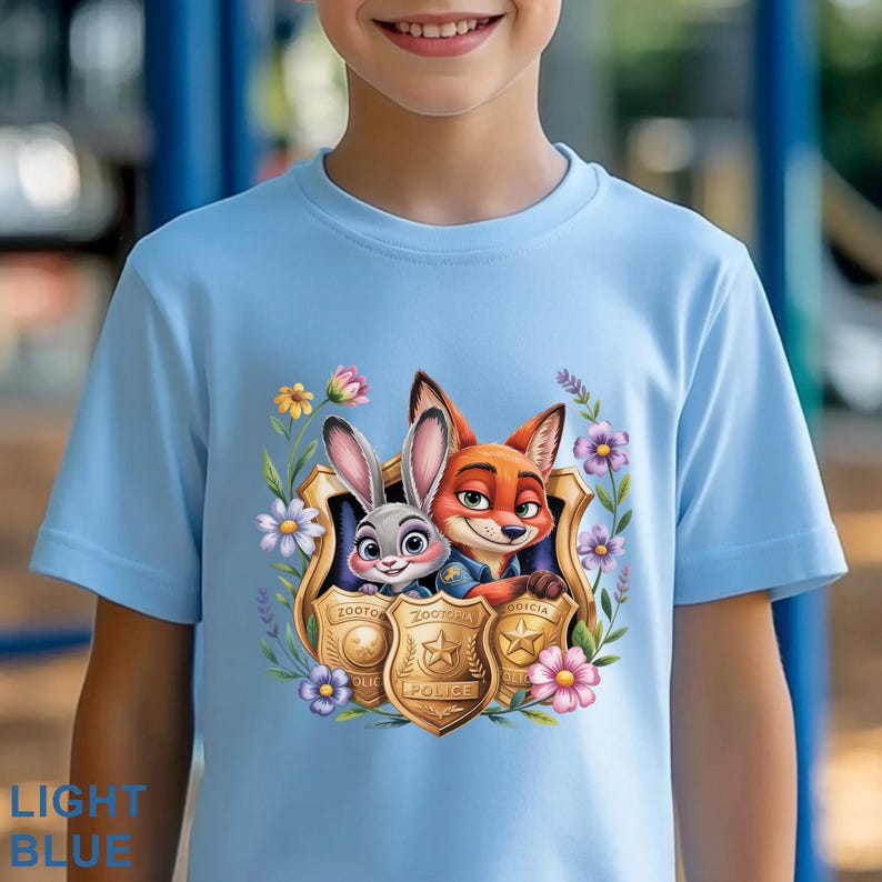 Puede incluir: Camiseta azul claro con una ilustraci&oacute;n de dibujos animados de Judy Hopps y Nick Wilde de Zootr&oacute;polis, enmarcada por flores y placas de polic&iacute;a. La camiseta tiene cuello redondo y mangas cortas. El texto "LIGHT BLUE" est&aacute; abajo a la izquierda.