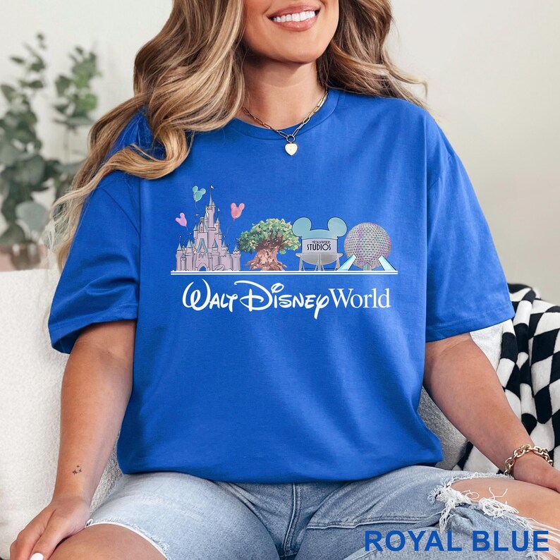 May include: Royal blue t-shirt featuring a Walt Disney World graphic. The design includes a castle, tree, Mickey Mouse ears, and a sphere. The text "Walt Disney World" is printed below the graphic.