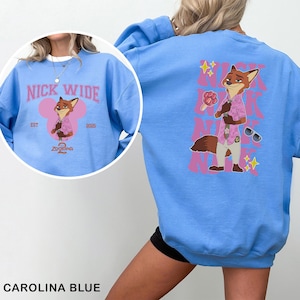 May include: Carolina blue sweatshirt featuring a cartoon fox character in a pink shirt and sunglasses. The front design includes text "NICK WIDE" and "Zootopia". The back design repeats the fox character and text "NICK WIDE".