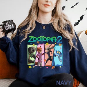 Może przedstawiać: Granatowa bluza z napisem "ZOOTOPIA 2" w kolorze zielono-białym. Projekt zawiera wizerunki postaci z filmu. Słowo "NAVY" jest wydrukowane na dole bluzy.