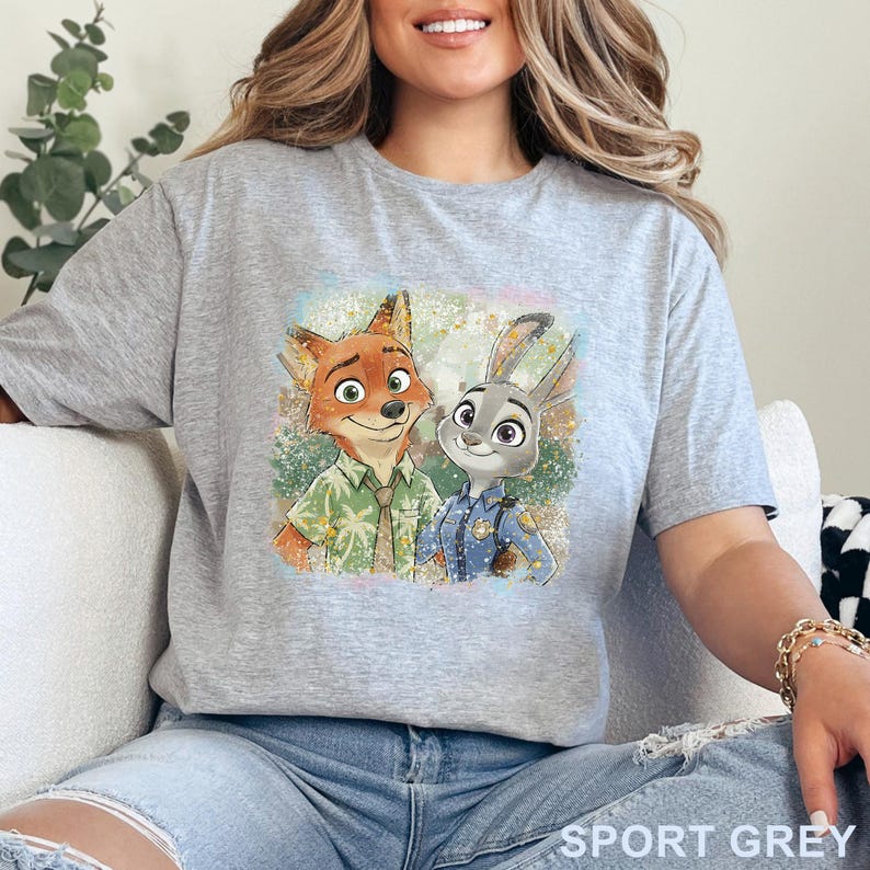 K&ouml;nnte beinhalten: Sportgraues T-Shirt mit farbenfroher Grafik von Nick Wilde und Judy Hopps aus Zoomania. Nick tr&auml;gt ein gr&uuml;nes Hemd und Judy eine Polizeiuniform. Das Shirt besteht aus weichem Material.