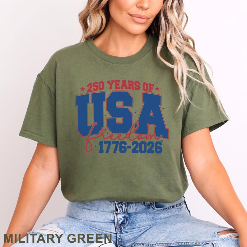 May include: Military green t-shirt with the text "250 YEARS OF USA Freedom 1776-2026" in blue and red. The shirt has a crew neck and short sleeves.