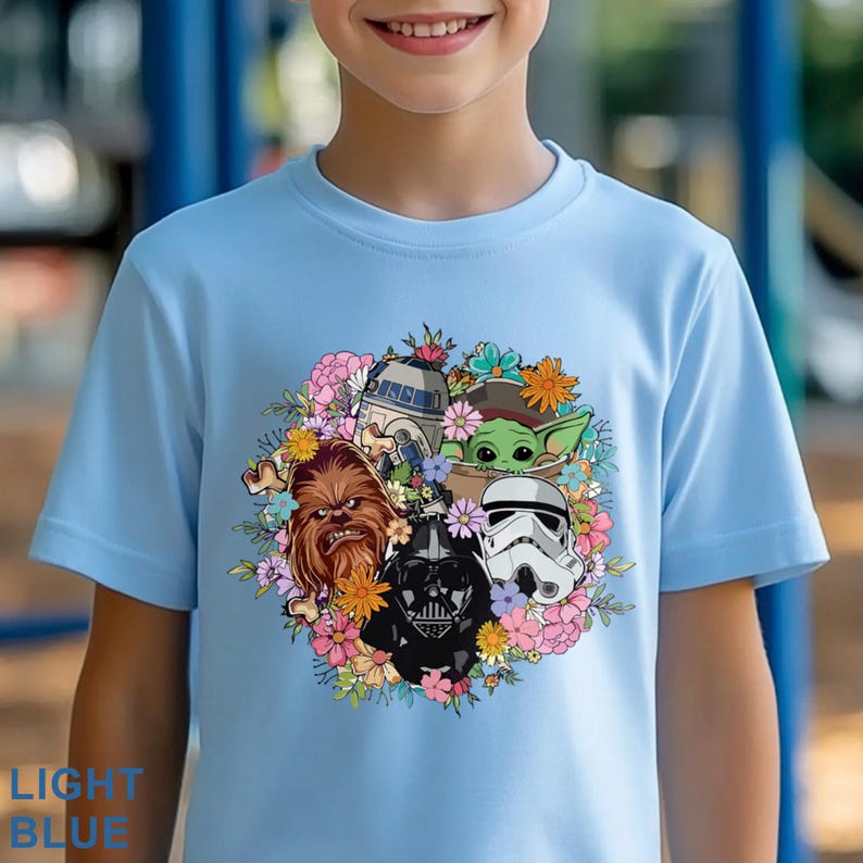 Puede incluir: Camiseta azul claro con un dise&ntilde;o floral colorido con personajes de Star Wars, incluyendo Darth Vader, Chewbacca y Baby Yoda. La camiseta tiene mangas cortas y el texto "LIGHT BLUE" est&aacute; impreso en la parte inferior.