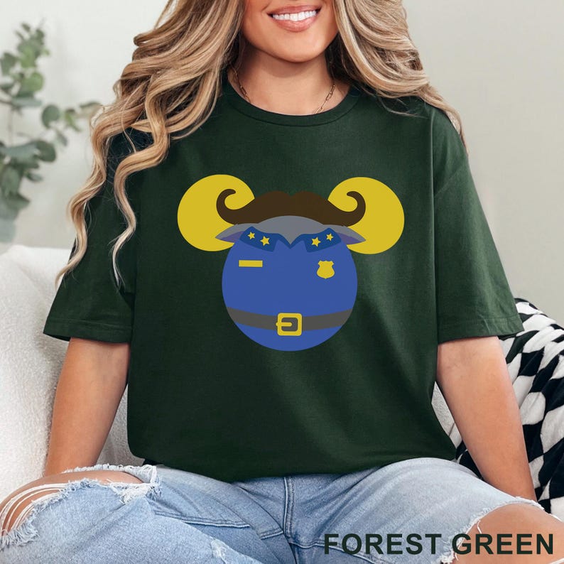 Puede incluir: Camiseta verde bosque con una cabeza de carnero de dibujos animados con uniforme de polic&iacute;a. El carnero tiene cuernos amarillos, un bigote marr&oacute;n y un uniforme de polic&iacute;a azul con una hebilla dorada. El texto "FOREST GREEN" est&aacute; en la parte inferior de la imagen.