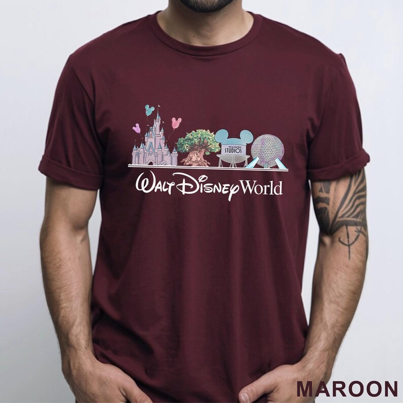 May include: Maroon t-shirt featuring a graphic of Walt Disney World landmarks, including a castle, tree, Mickey Mouse ears, and a sphere. The words "Walt Disney World" are printed in white below the graphic. The shirt is a solid maroon color.