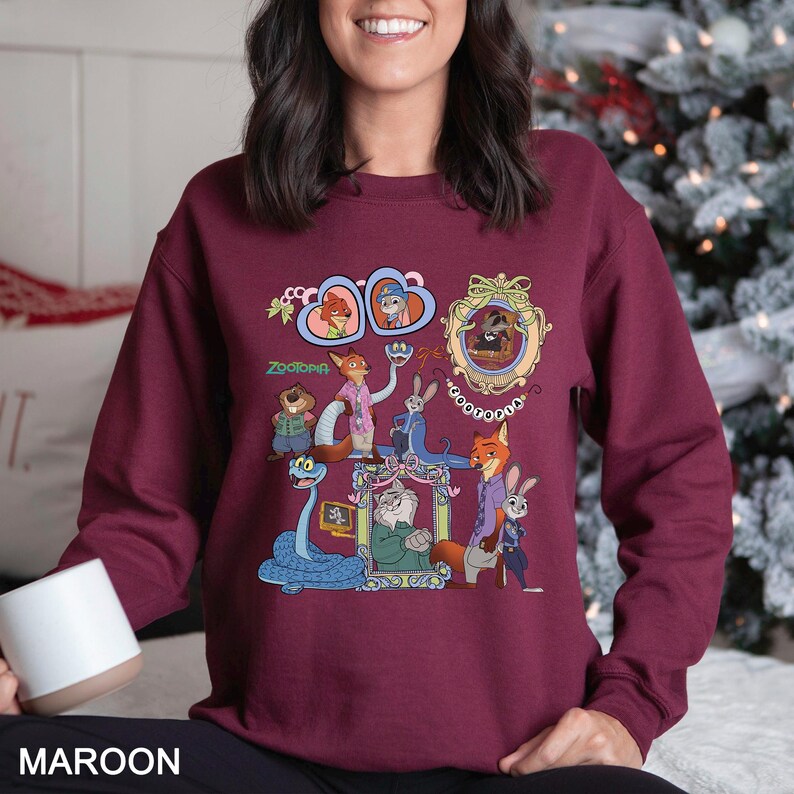 May include: Maroon sweatshirt featuring a colorful graphic of characters from the animated movie Zootopia. The design includes framed portraits and cartoon illustrations of various animals. The word "Zootopia" is also printed on the sweatshirt.