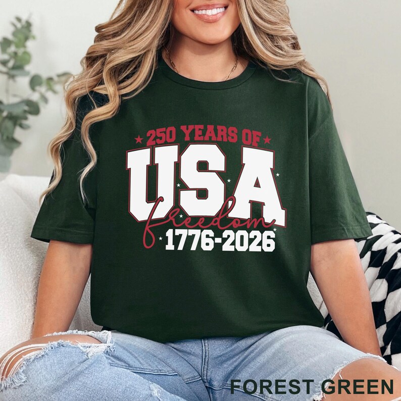 May include: Forest green t-shirt with the text "250 YEARS OF USA freedom 1776-2026" in white and red. The shirt is a crew neck and is being worn by a person.