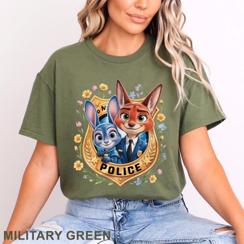 Peut inclure: T-shirt vert militaire avec une image de dessin anim&eacute; d'un renard et d'un lapin en uniforme de police, sur un badge dor&eacute; avec le mot "POLICE". Le motif est entour&eacute; de fleurs.