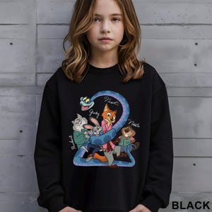 K&ouml;nnte beinhalten: Schwarzes Sweatshirt mit einer Cartoon-Grafik von Filmfiguren, darunter ein Fuchs, ein Hase und ein Biber, mit den Namen "Judy", "Nick" und "Nibbles". Das Wort "BLACK" ist unten rechts in Wei&szlig; aufgedruckt.