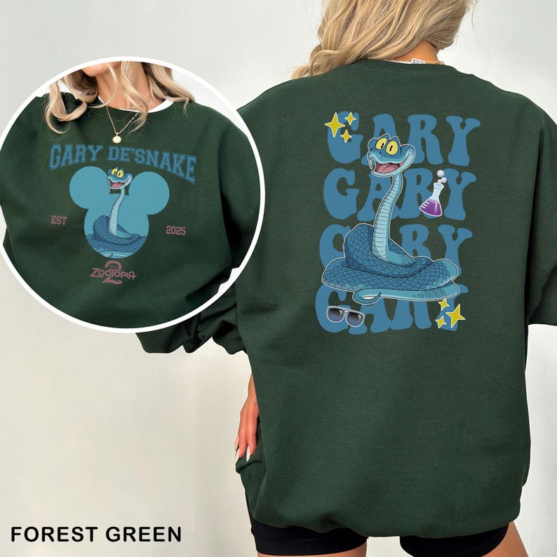 May include: Forest green sweatshirt featuring a cartoon snake character with the text "GARY DE'SNAKE" and "ZOOTOPIA 2". The back of the sweatshirt repeats the name "GARY" with the snake graphic, sunglasses, and stars. The sweatshirt is a crew neck.