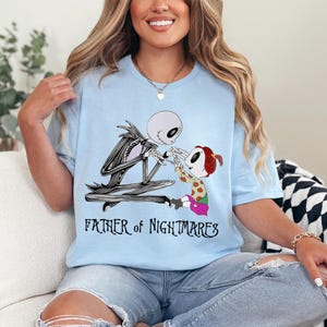 Puede incluir: Camiseta azul claro con una ilustraci&oacute;n de dibujos animados de Jack Skellington y un ni&ntilde;o de The Nightmare Before Christmas. El texto "FATHER of NIGHTMARES" est&aacute; debajo de la imagen.