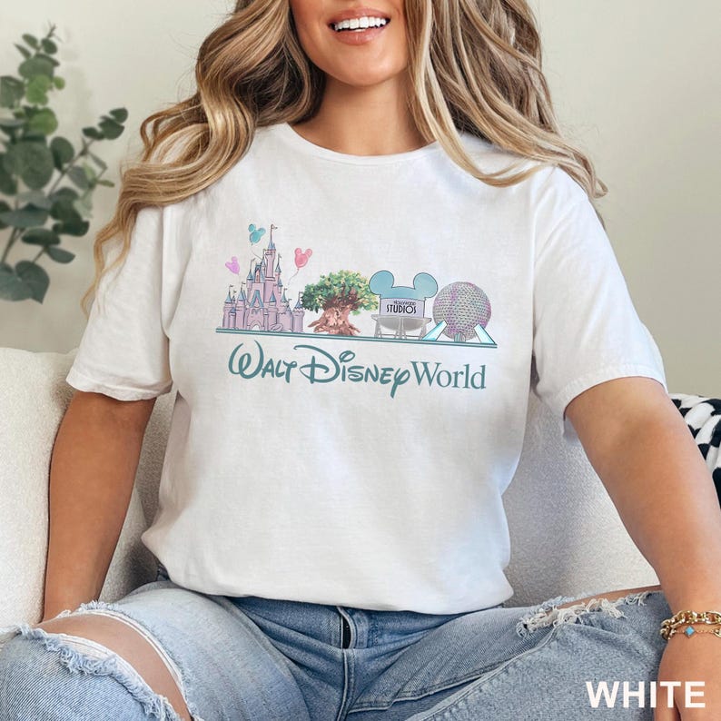May include: White t-shirt featuring a pastel illustration of Walt Disney World landmarks, including Cinderella's castle, the Tree of Life, and Spaceship Earth. The words "Walt Disney World" are printed below the graphic. The shirt is made of a soft material.