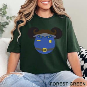 Puede incluir: Camiseta verde bosque con un dise&ntilde;o de polic&iacute;a de dibujos animados. El dise&ntilde;o incluye una cara azul con una placa, una hebilla dorada y un bigote marr&oacute;n. El texto "FOREST GREEN" est&aacute; en la parte inferior.